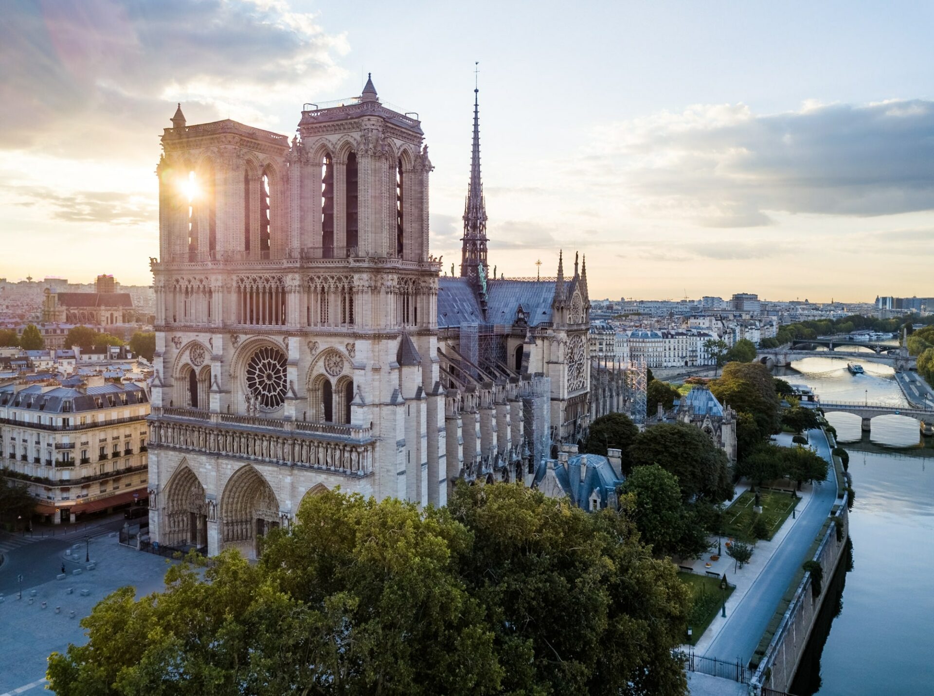 Vue drone rapprochée de Notre-Dame de Paris, avec le soleil levant entre une tour. 